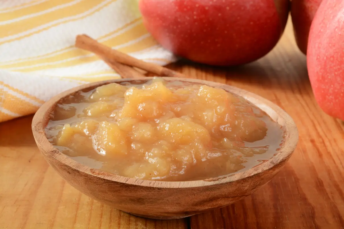 "Bowl of homemade cinnamon applesauce on a rustic kitchen table.