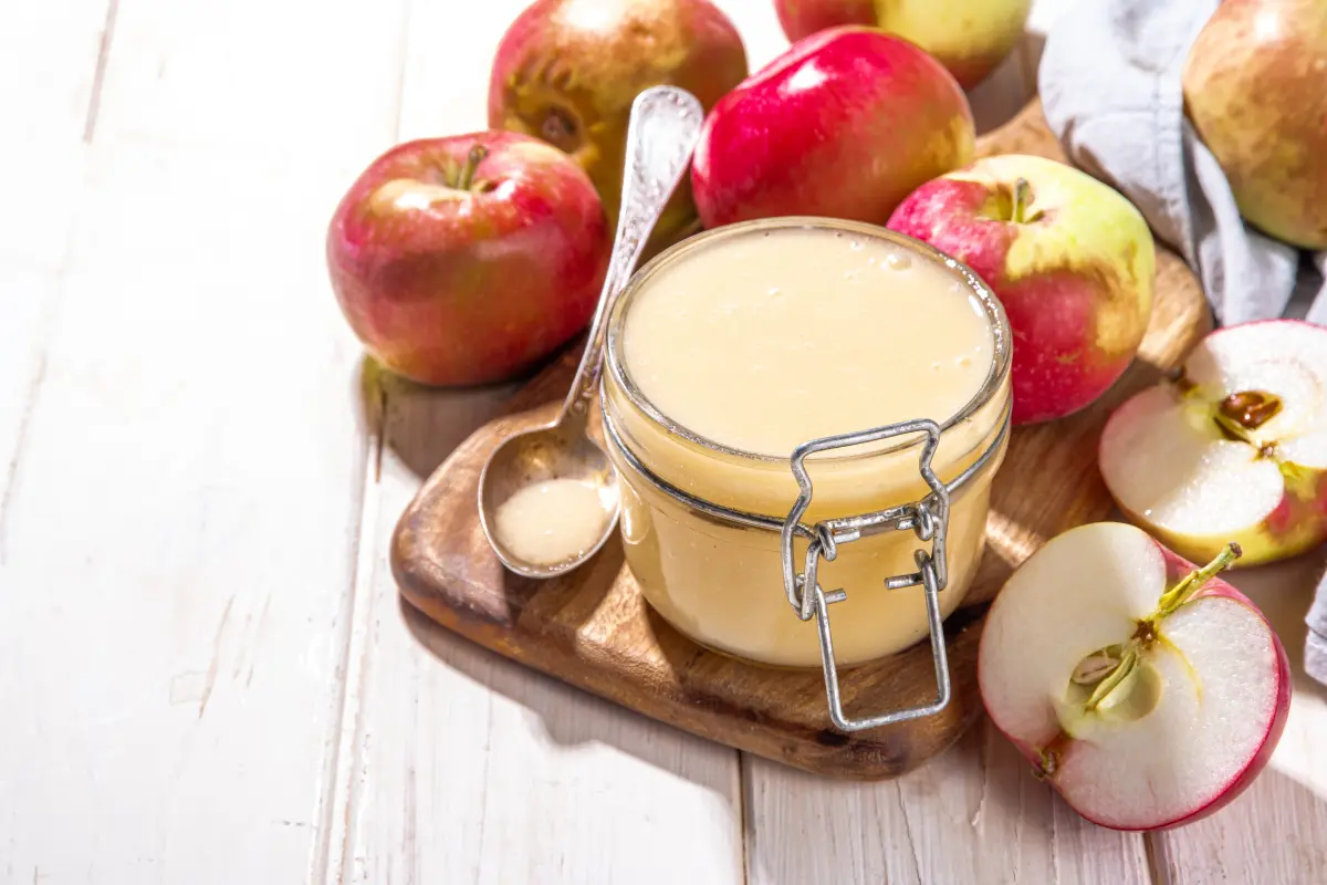 Homemade applesauce in a bowl with fresh apples in the background.